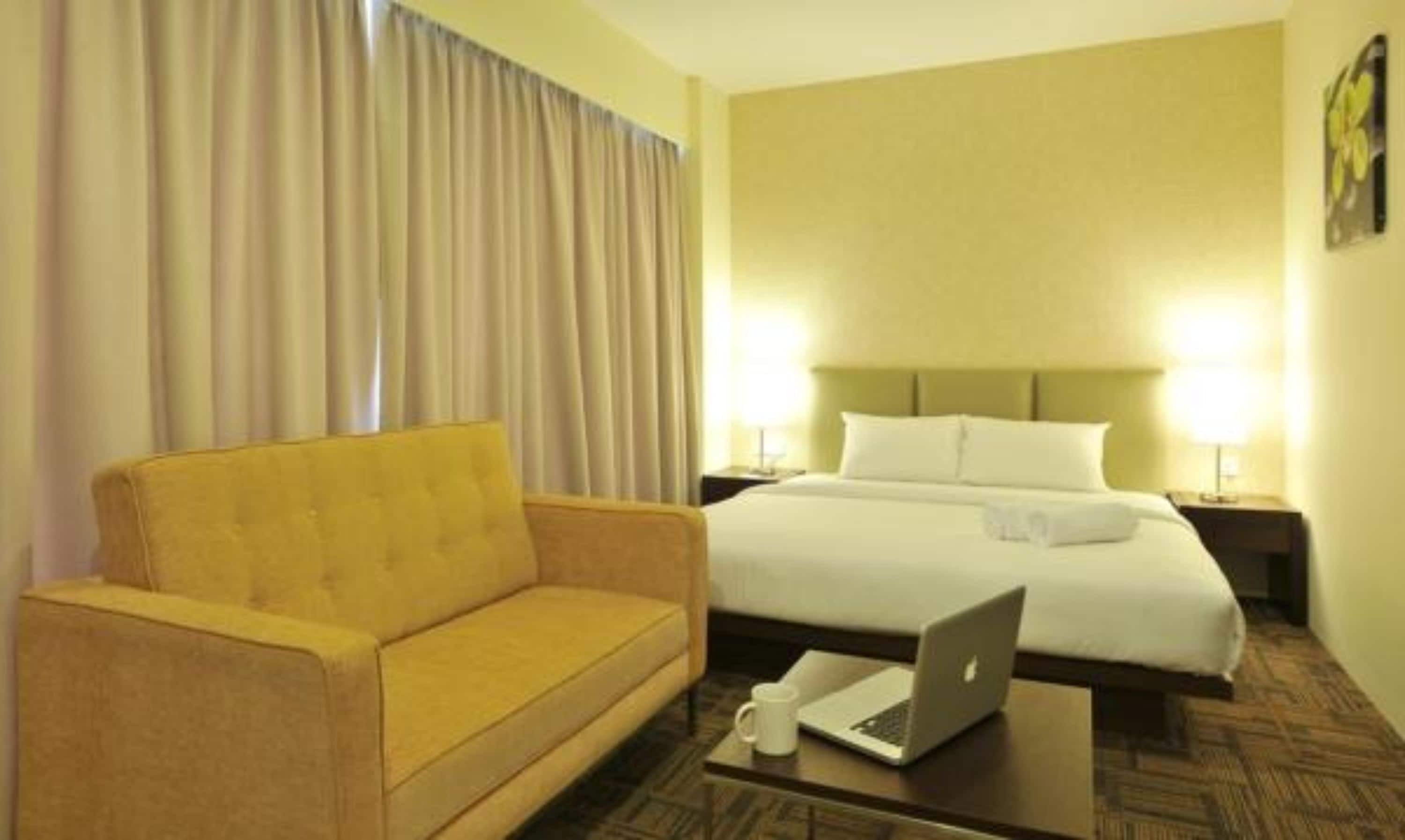 Ein Hotelzimmer mit einem Bett, einem gelben Sofa, einem Couchtisch mit einem Laptop und einer Lampe.