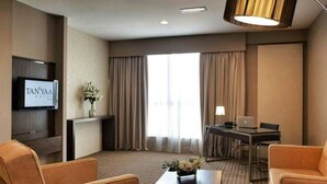 A hotel room with a TV, a desk with a lamp, a sofa, and a large window with curtains. - Hotel Primera Suite (Cyberjaya)