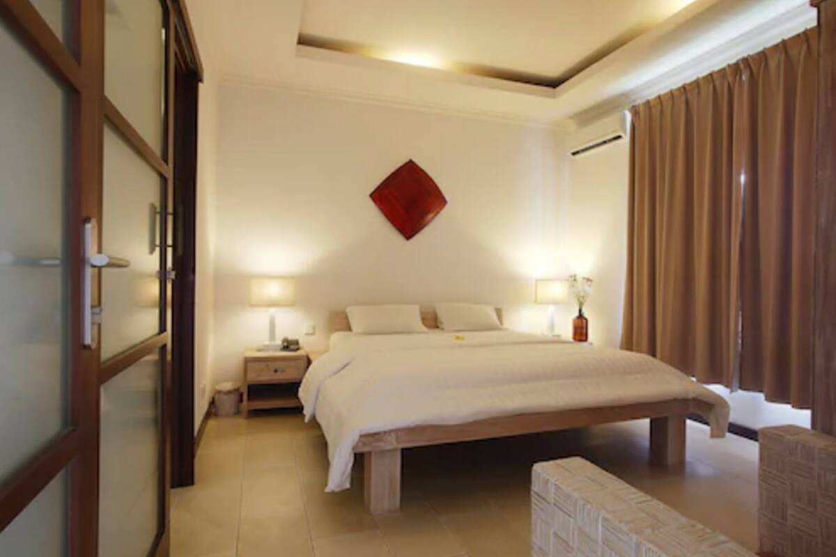 A bedroom with a large bed, bedside lamps, a nightstand, a wooden bench, and a red accent wall.
