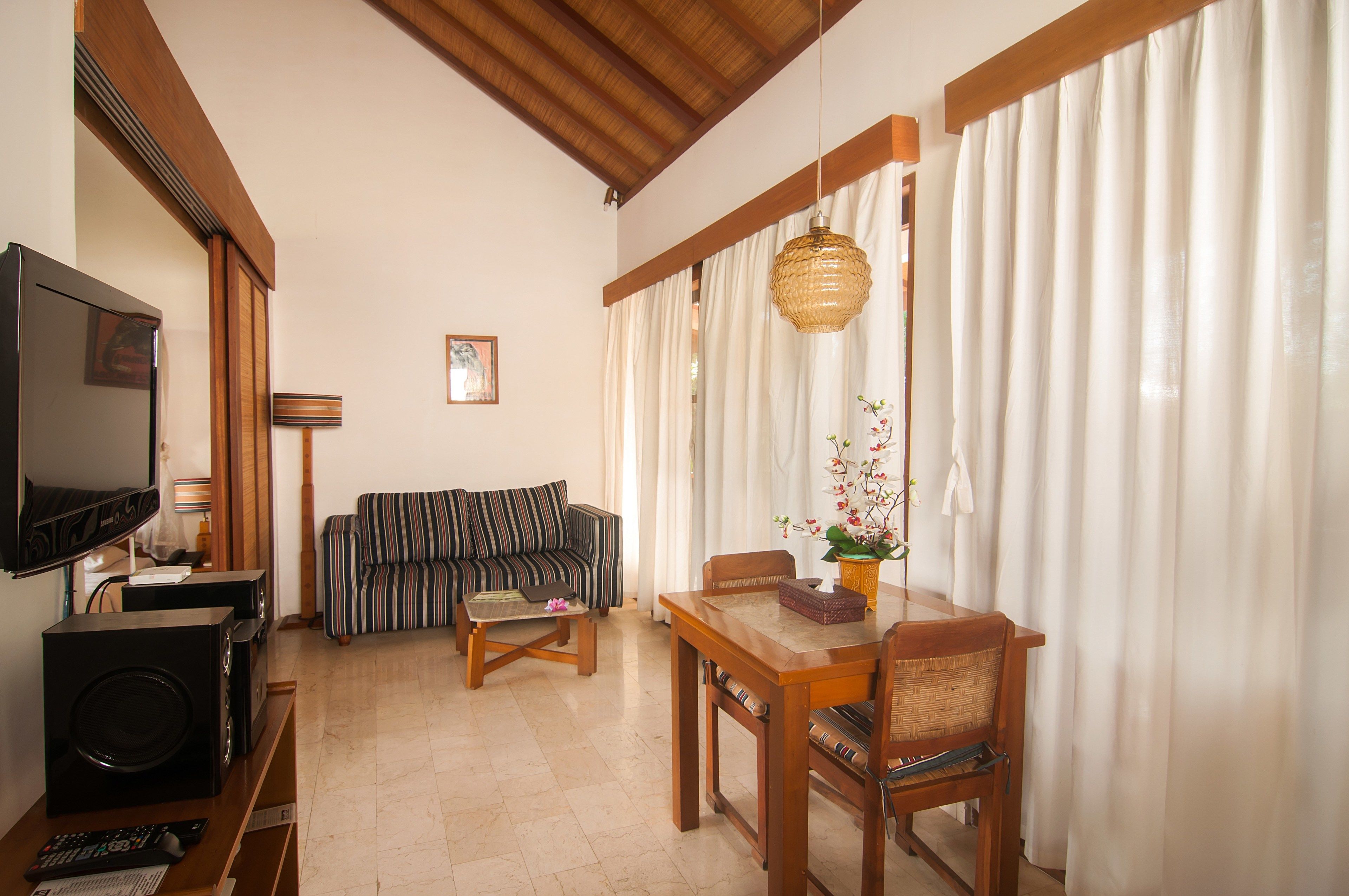 Una sala de estar con televisor, sofá, mesa de comedor y cortinas.