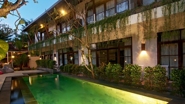 A hotel with a swimming pool, greenery, and a well-lit exterior at dusk. - The Studio (Seminyak)