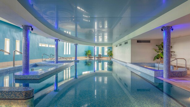 Une piscine intérieure à l’eau d’un bleu limpide, avec des murs carrelés et un éclairage bleu.