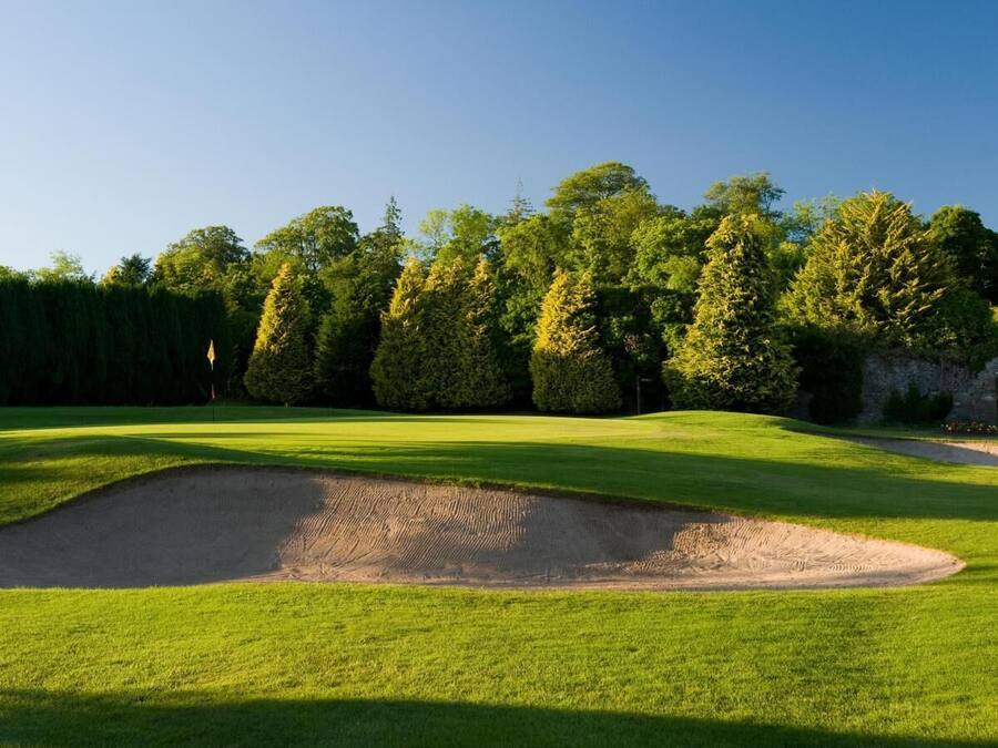 Un campo de golf con un búnker de arena, césped bien cuidado y un arco de piedra.