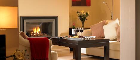 A cozy living room with a fireplace, a sofa, a coffee table, and a dining table set for a meal.