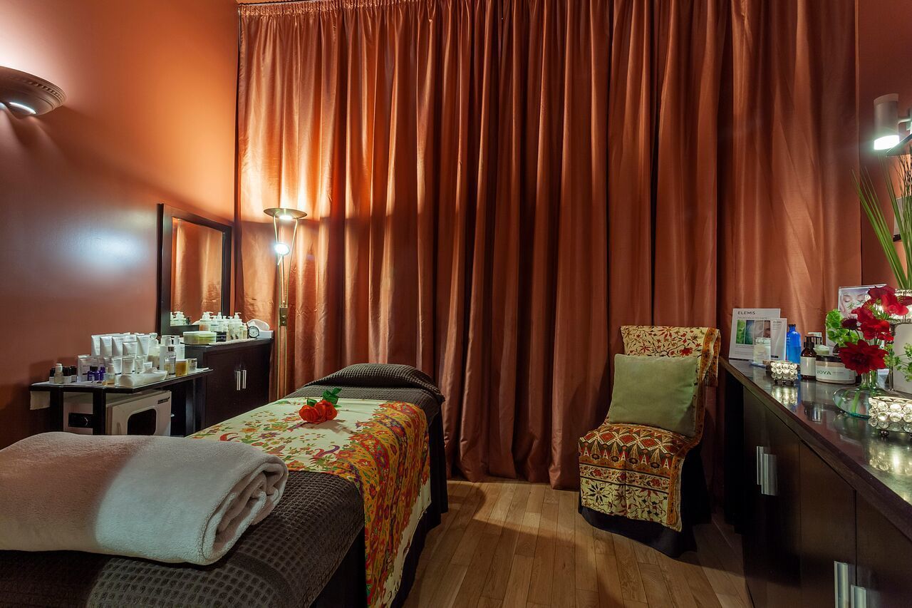 A hotel room with a bed, a chair, a desk with toiletries, and a mirror.