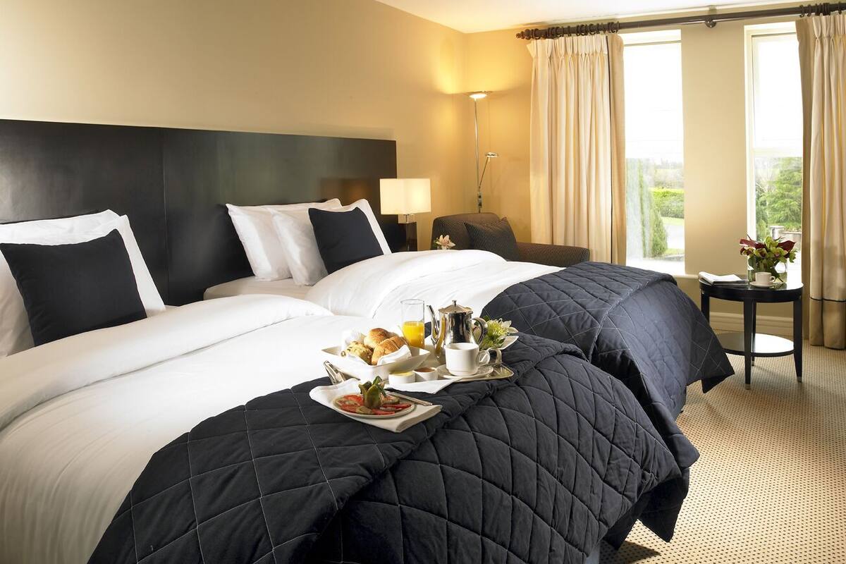 Une chambre d’hôtel avec un grand lit, une table de chevet avec une lampe et une vue sur l’extérieur par la fenêtre.