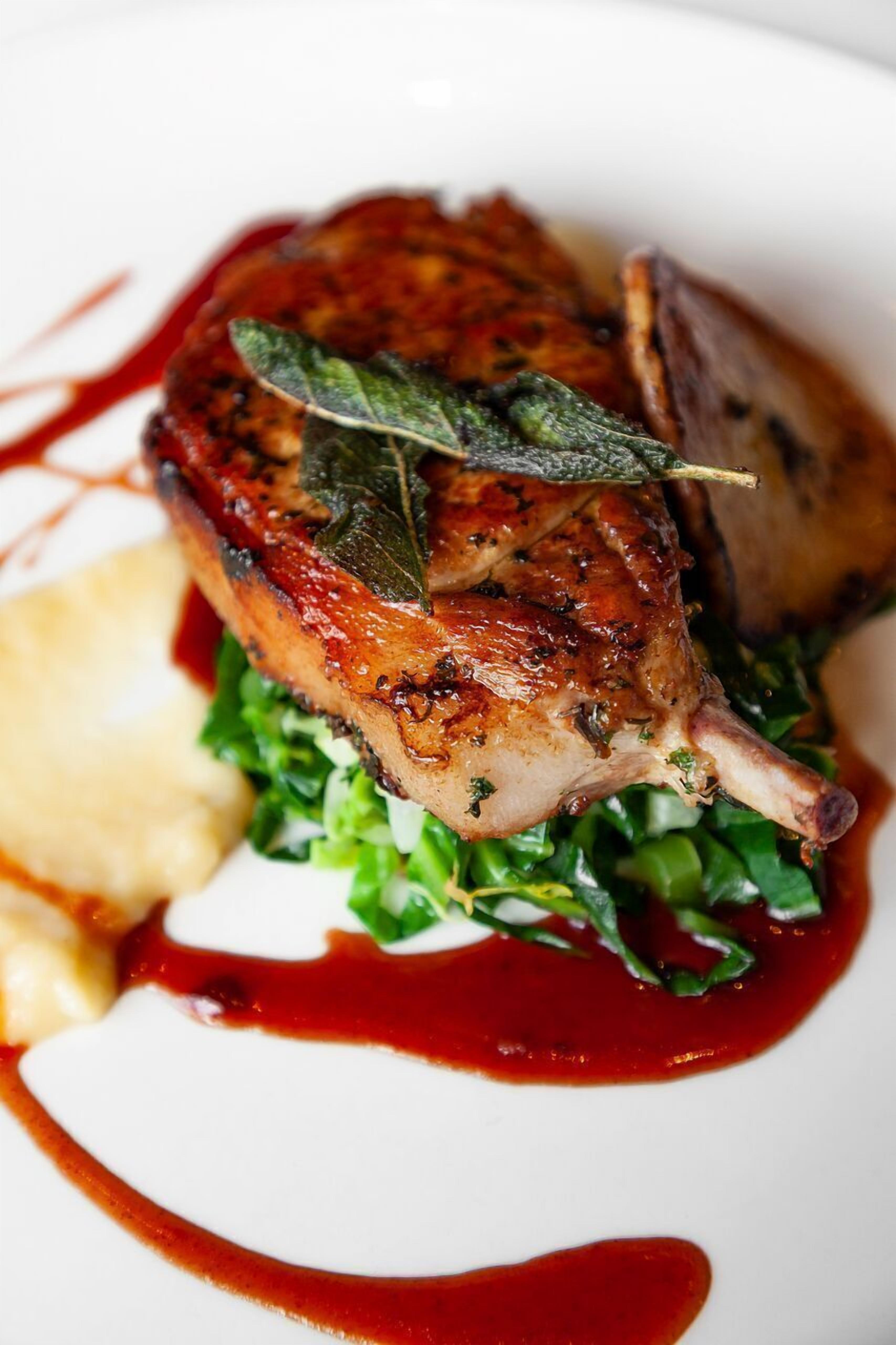 A plate with a roasted duck, greens, and a red sauce.