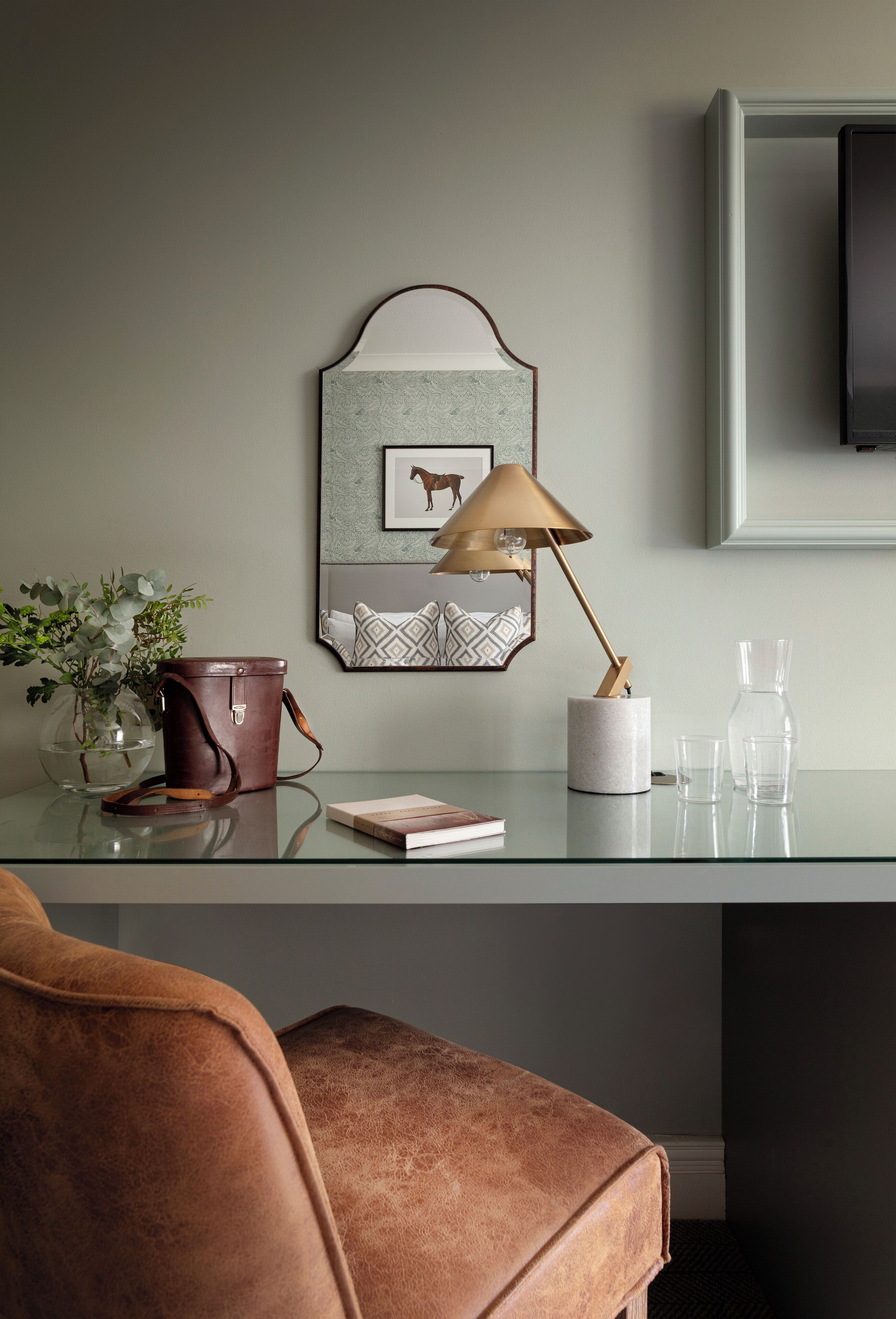 A modern room with a glass desk, leather chair, and a mounted TV.