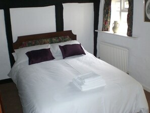 A neatly made bed with white linens and two purple pillows, a wooden headboard with floral patterns, and a white radiator on the wall.