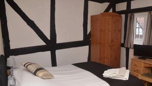 A bedroom with a bed, a wooden wardrobe, a television on a wooden dresser, and a window with curtains.