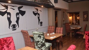 A restaurant interior with wooden tables and chairs, a high ceiling with exposed beams, and a wall with a bull's head mural.