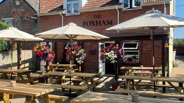 Un pub llamado "The Foxham" con terraza y arreglos florales.