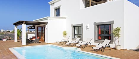 A modern two-story house with a swimming pool, outdoor seating, and a pergola.