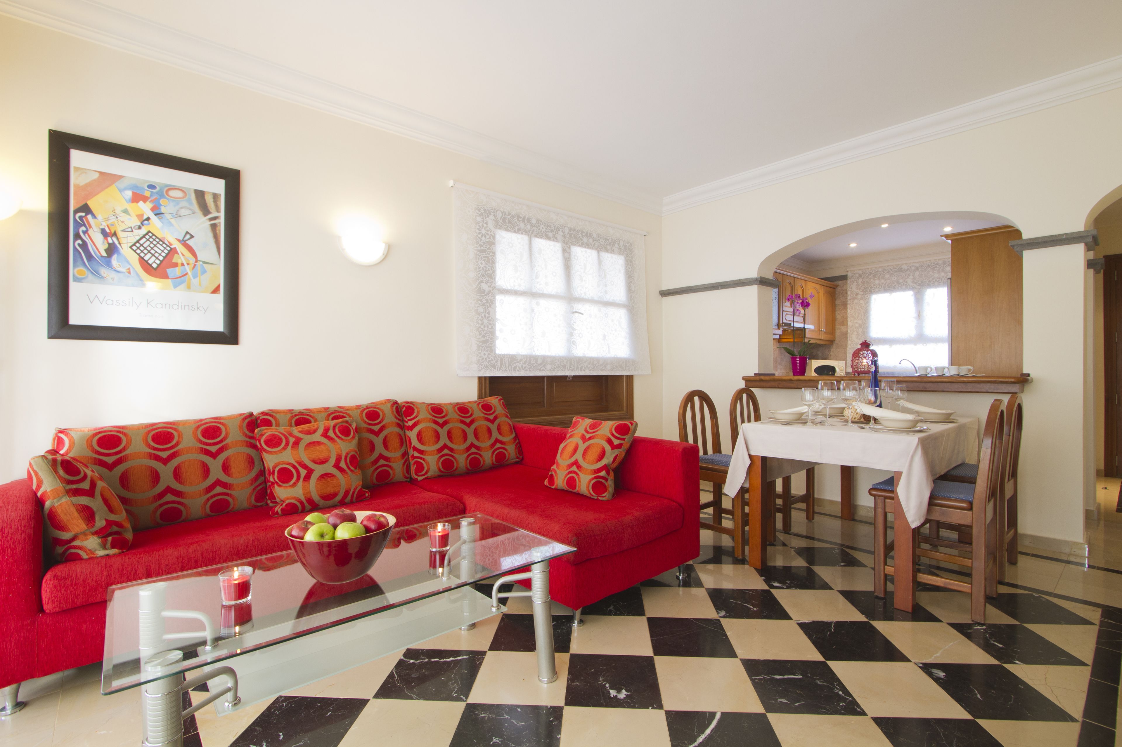 A living room with a red sofa, a glass coffee table, and a dining area with a table set for four.