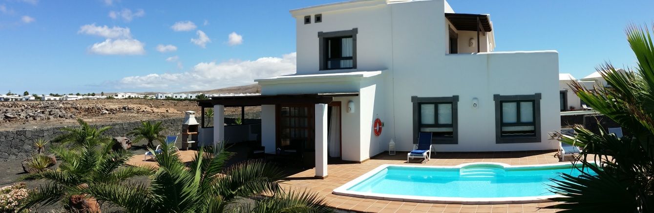 Et moderne hus med to etager, en swimmingpool, en overdækket terrasse og udsigt til stranden.