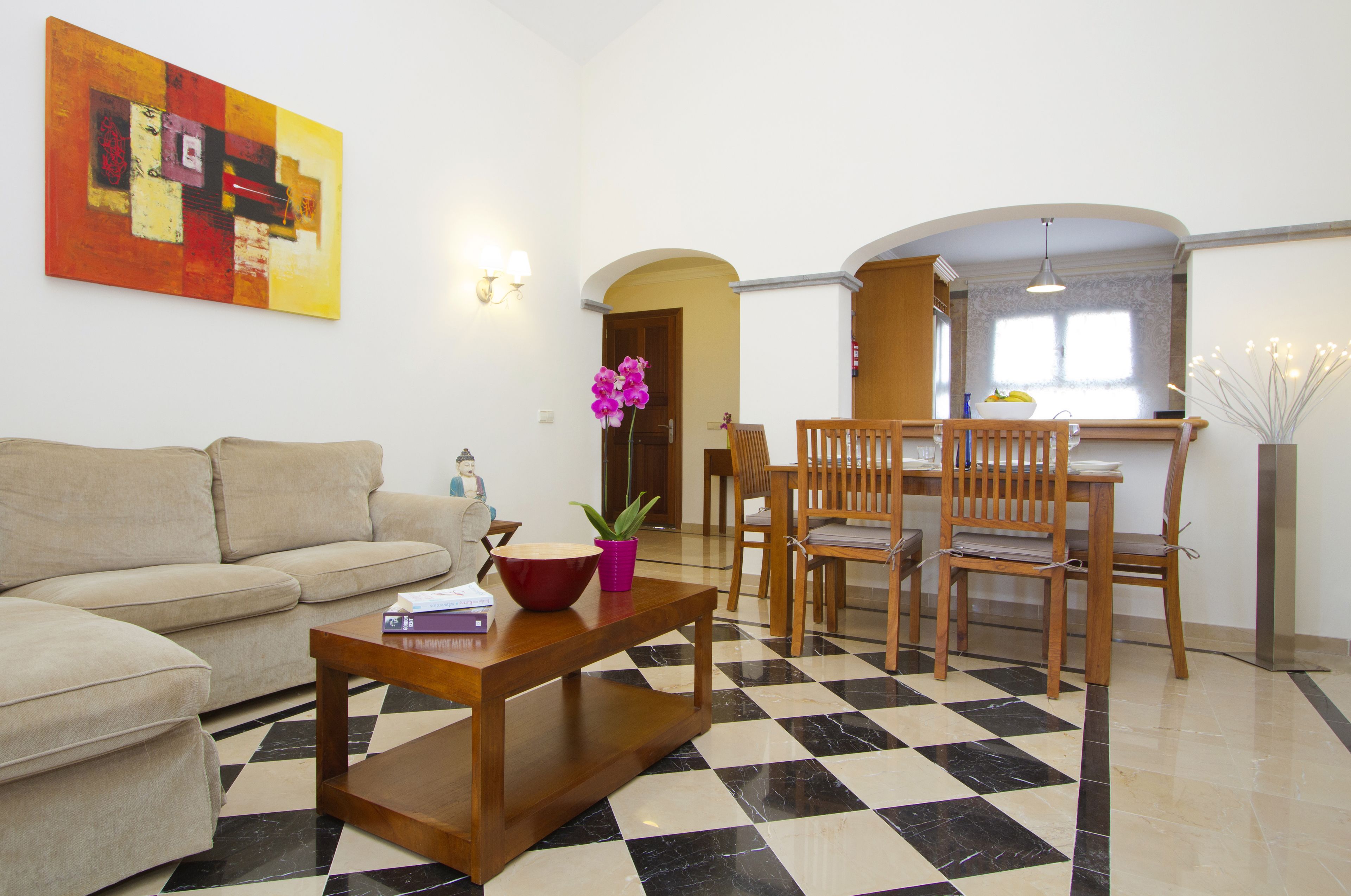 A living room with a checkered floor, a sofa, a wooden coffee table, and a dining area with wooden chairs and a table.