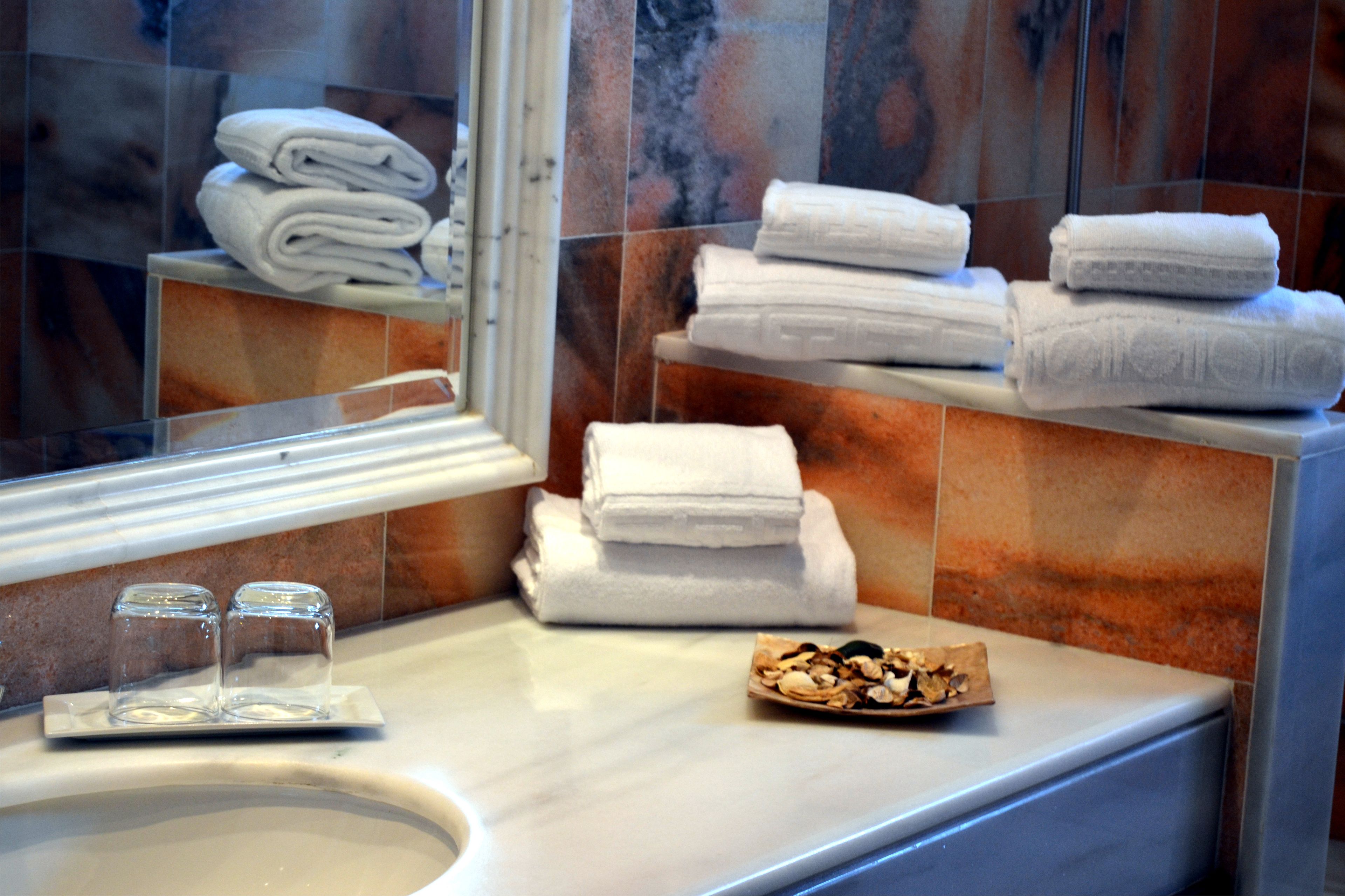 Un bany amb un lavabo de marbre, tovalloles blanques apilades i una safata amb fruits secs.