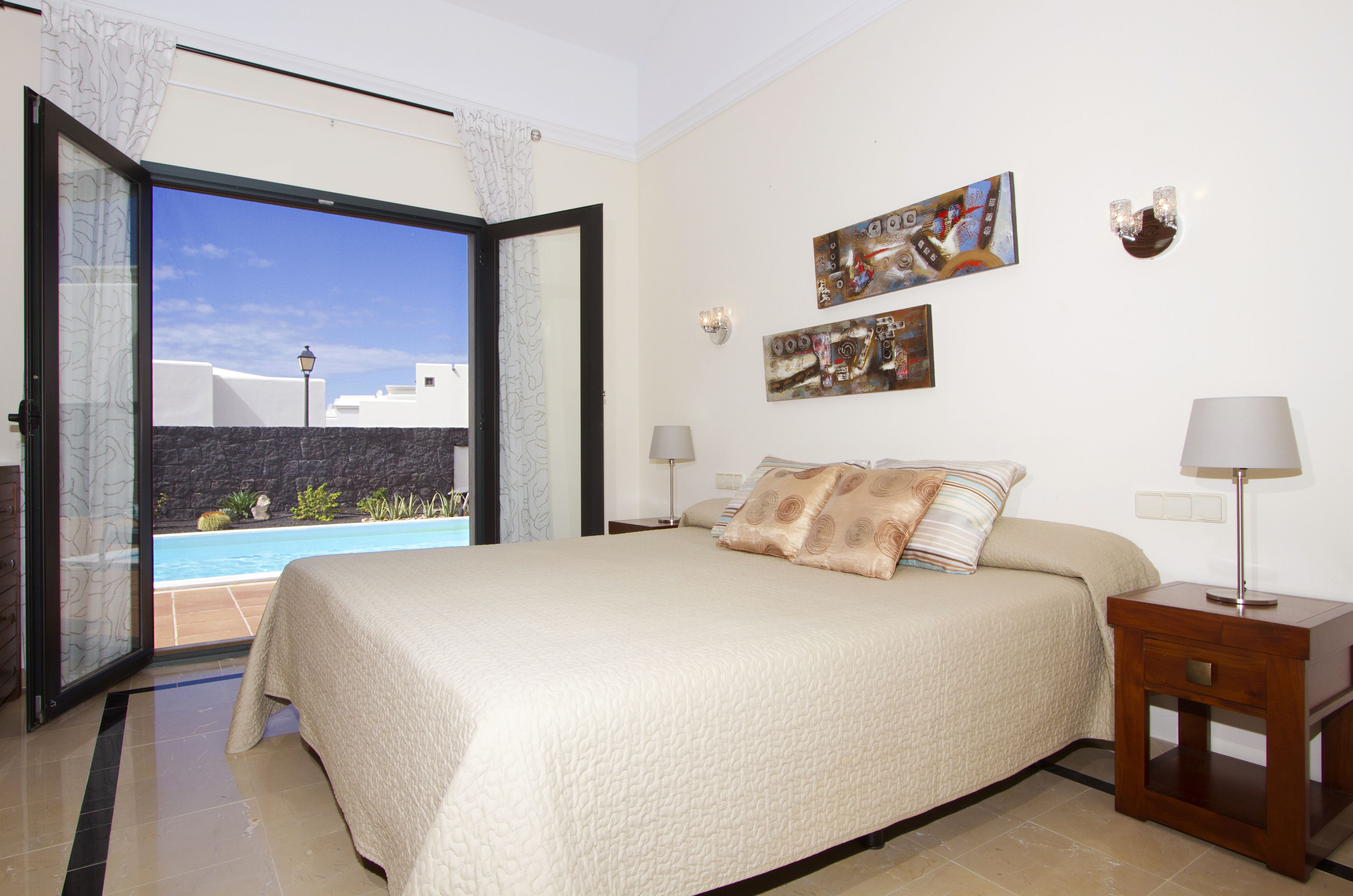 Une chambre avec un grand lit, une table de chevet, une lampe et une vue sur une piscine.