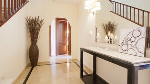 A hallway with a wooden staircase, a large vase, a console table with candles, and a painting. - Villas Coral Deluxe (Yaiza)