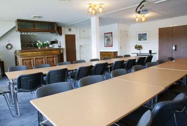 Un salón de conferencias con una larga mesa, sillas, un proyector y una zona de cocina con armarios y un lavamanos.