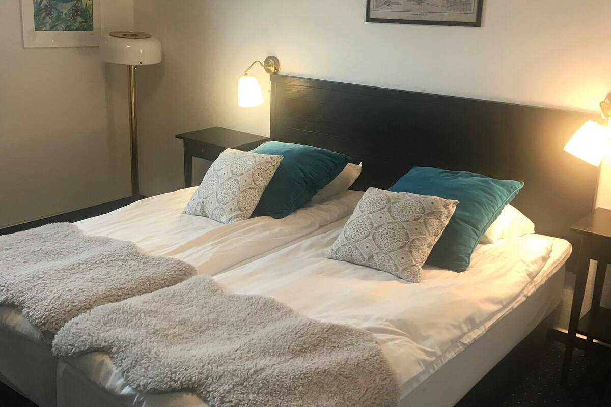A neatly made bed with patterned pillows and a fluffy blanket, two bedside lamps, a framed map on the wall, and a floor lamp.