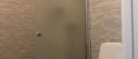 A bathroom with a glass shower enclosure, a toilet with a towel on the seat, and a wall with a brick pattern.