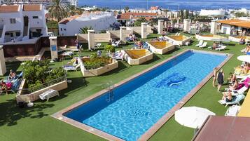 Relax by the resort pool, surrounded by lush greenery and palm trees, with a view of the sea in the background.