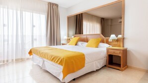 Une chambre d’hôtel avec un grand lit, une table de chevet, un miroir et des rideaux légers.