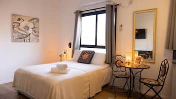 A hotel room with a bed, a small table with a lamp, a chair, a mirror, and a painting on the wall.