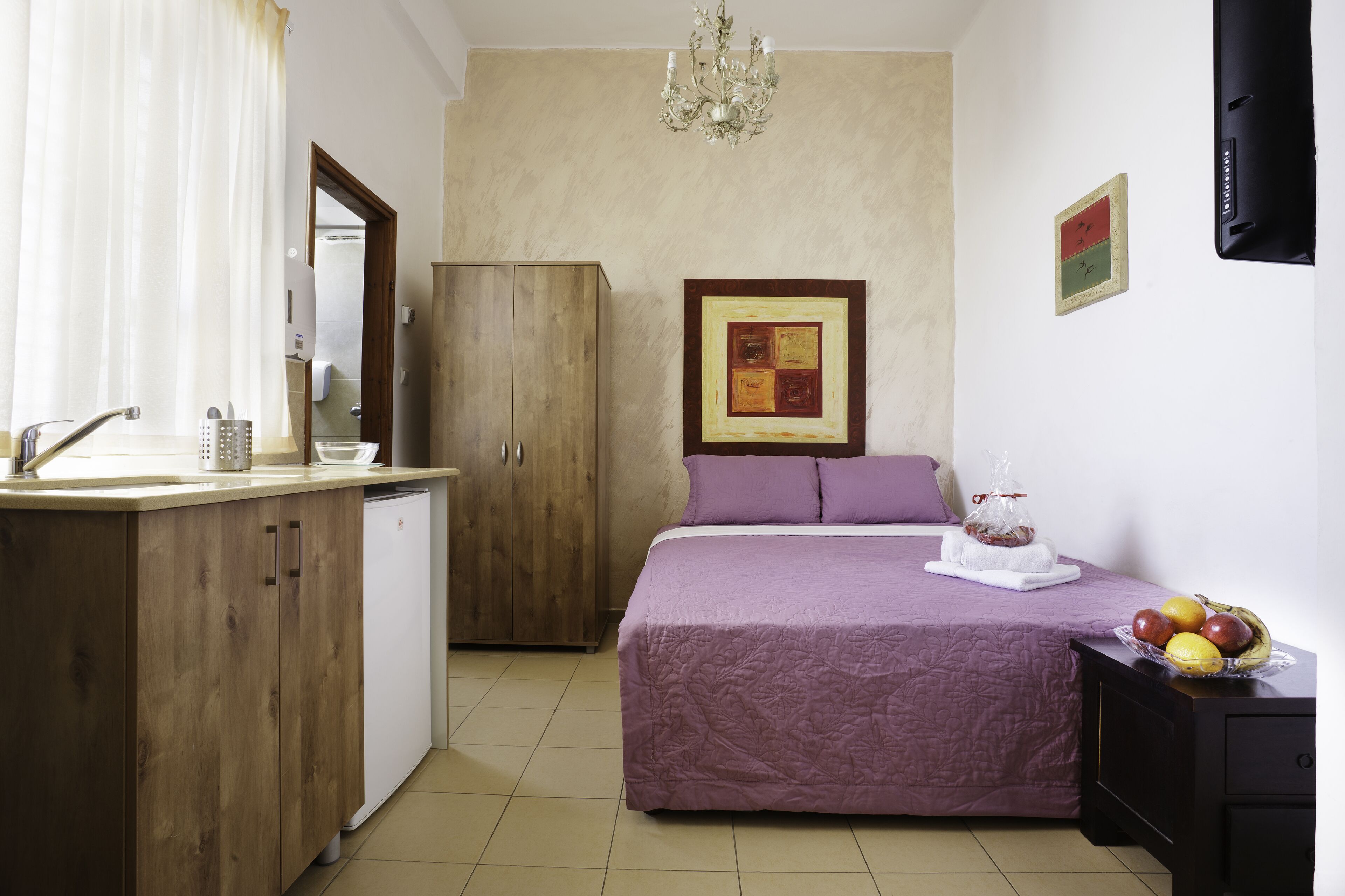 A bedroom with a bed, a bedside table with fruits, a wardrobe, and a bathroom visible through an open door.