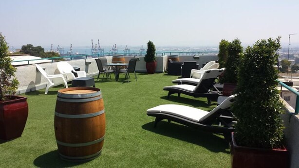 Een terras op het dak met kunstgras, lounge fauteuils, een houten vat en potplanten.
