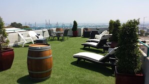 A rooftop terrace with artificial grass, lounge chairs, a wooden barrel, and potted plants. - City Center Apartments (Haifa)