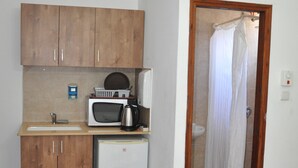 Een functionele keuken met houten kastjes, een magnetron, een kleine koelkast en een spoelbak.