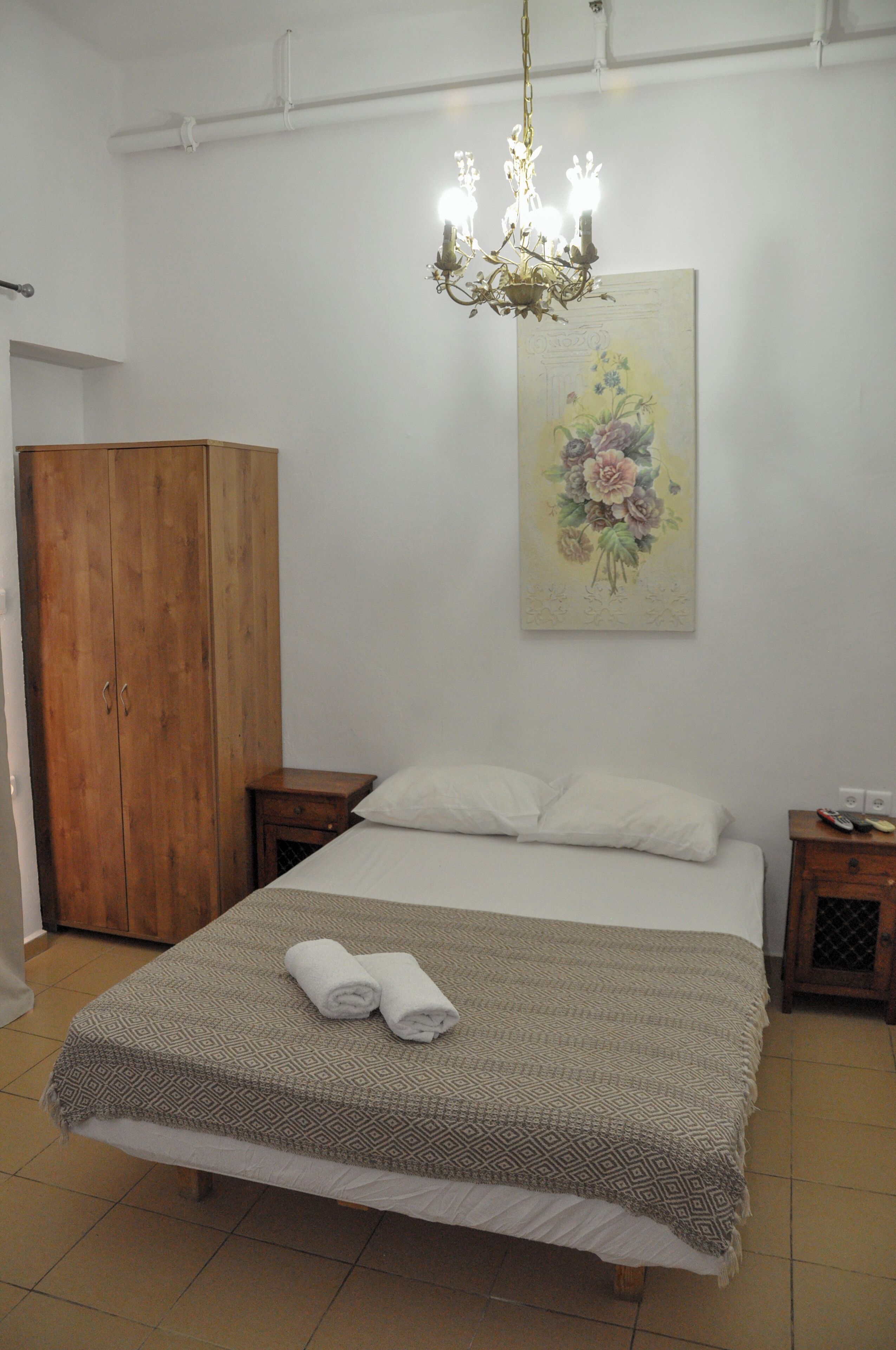 Ein Schlafzimmer mit einem Bett, einem Holzschrank, einem Nachttisch, einem an der Wand hängenden Gemälde und einer Chandelier.