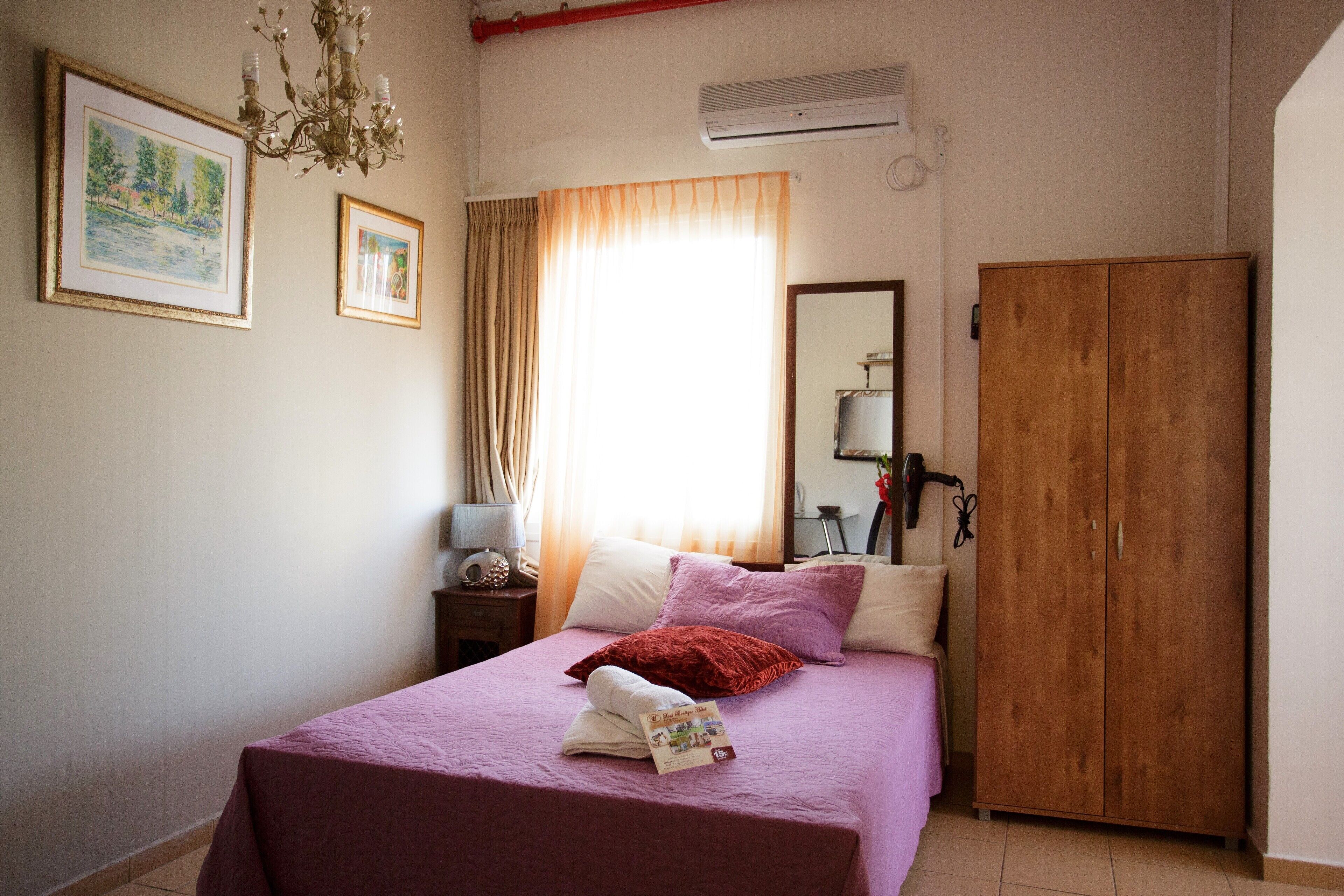 Un dormitorio con una cama, un armario de madera, una araña y dos cuadros en la pared.
