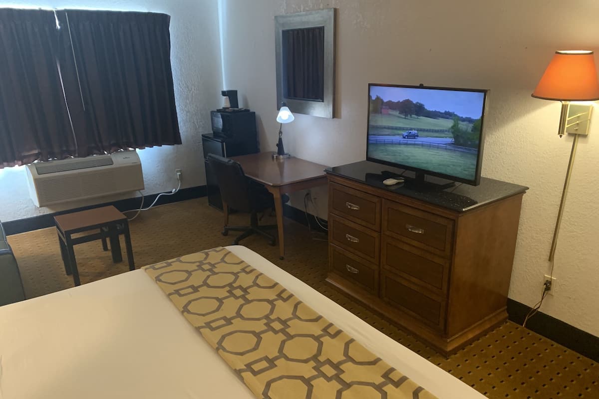 A hotel room with a bed, a desk, a television, a lamp, and a dresser.