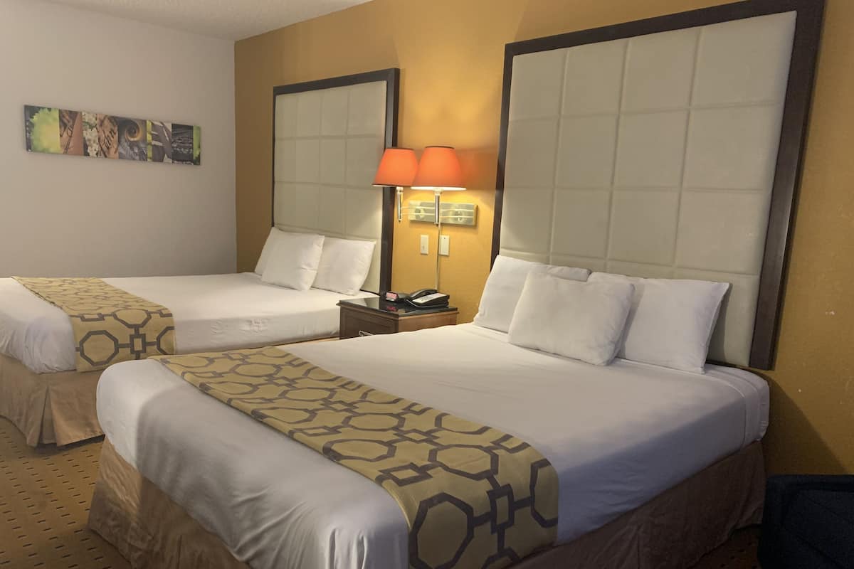 A hotel room with two beds, each with a headboard, a nightstand with a lamp, and a wall-mounted artwork.