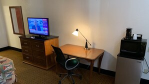 A hotel room with a wooden desk, a computer, a chair, a lamp, a microwave, and a refrigerator. - Brentwood Inn & Suites (Hobbs)
