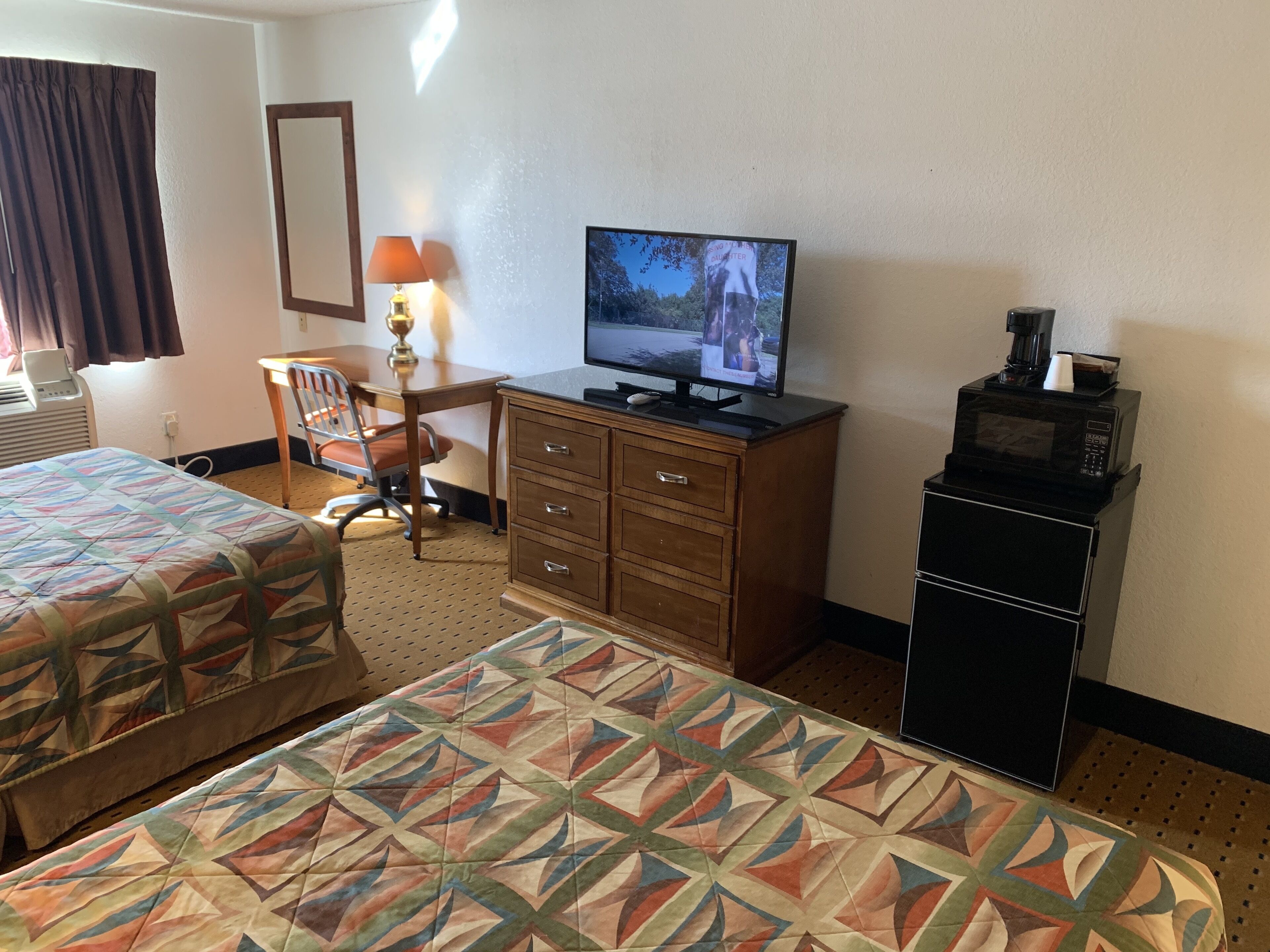 A hotel room with two beds, a desk with a lamp, a television, a microwave, and a small cabinet.