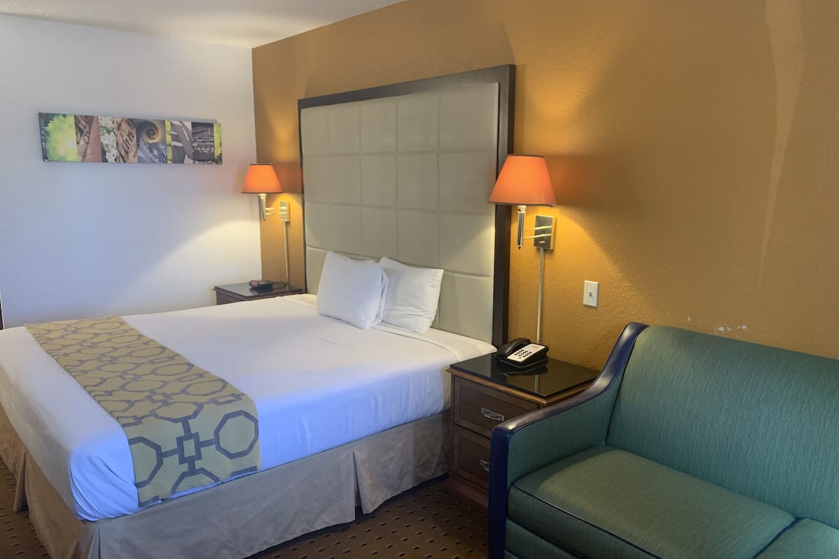 A hotel room with a large bed, two bedside lamps, a green armchair, and a small table.