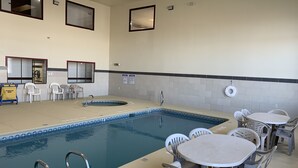 A pool area with a hot tub, lounge chairs, and a table with chairs. - Brentwood Inn & Suites (Hobbs)