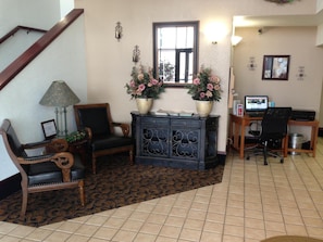 A living room with a staircase, a desk with a computer, and two flower vases on a cabinet. - Brentwood Inn & Suites (Hobbs)