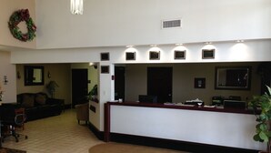 A reception area with a reception desk, a couch, a chair, and a potted plant. - Brentwood Inn & Suites (Hobbs)