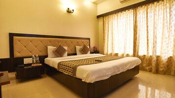 A hotel room with a large bed, a bedside table with a phone and water bottles, and a window with curtains.