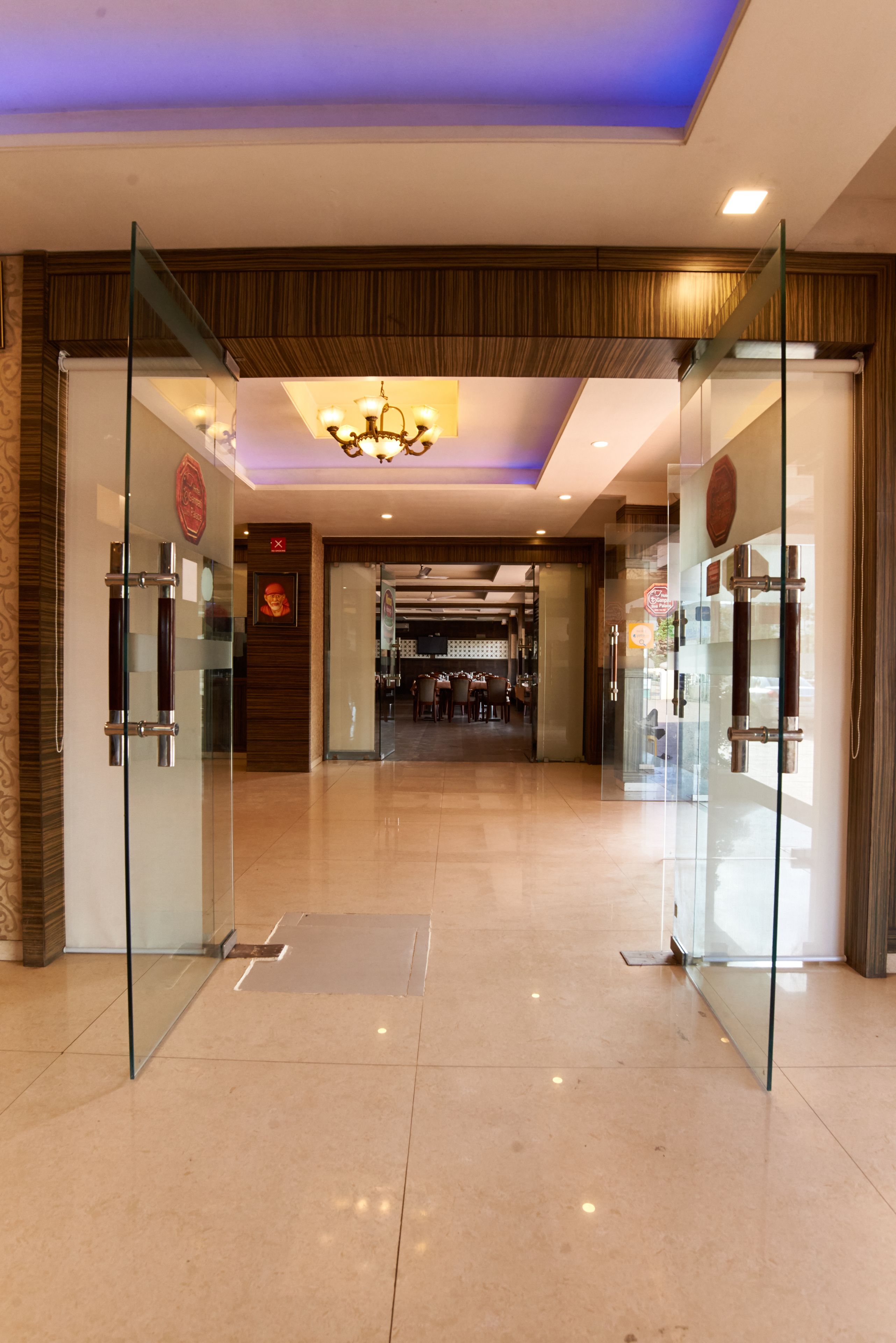 A hotel lobby with glass doors, a chandelier, and a tiled floor.