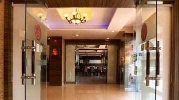 A hotel lobby with glass doors, a chandelier, and a tiled floor.