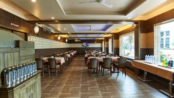 A restaurant with multiple tables and chairs, a kitchen area, and a television screen.