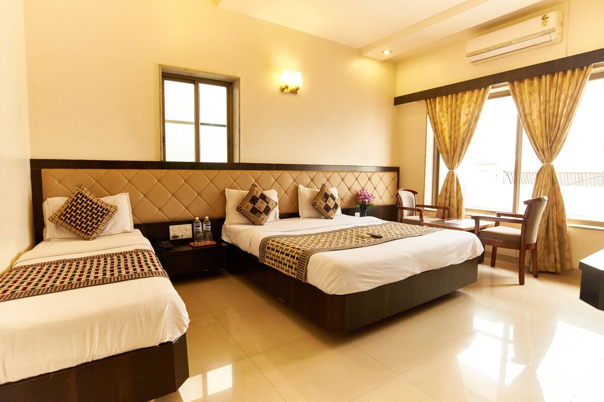 A hotel room with two beds, a desk, a chair, a window with curtains, and an air conditioning unit.