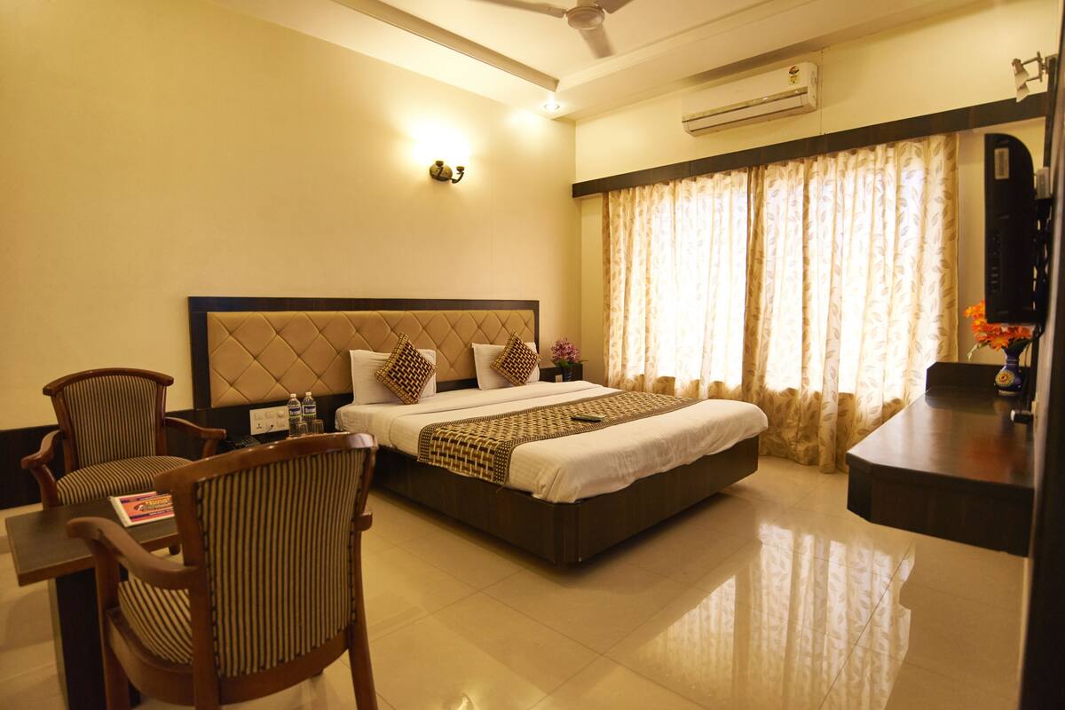 A hotel room with a bed, two chairs, a desk, and a television.