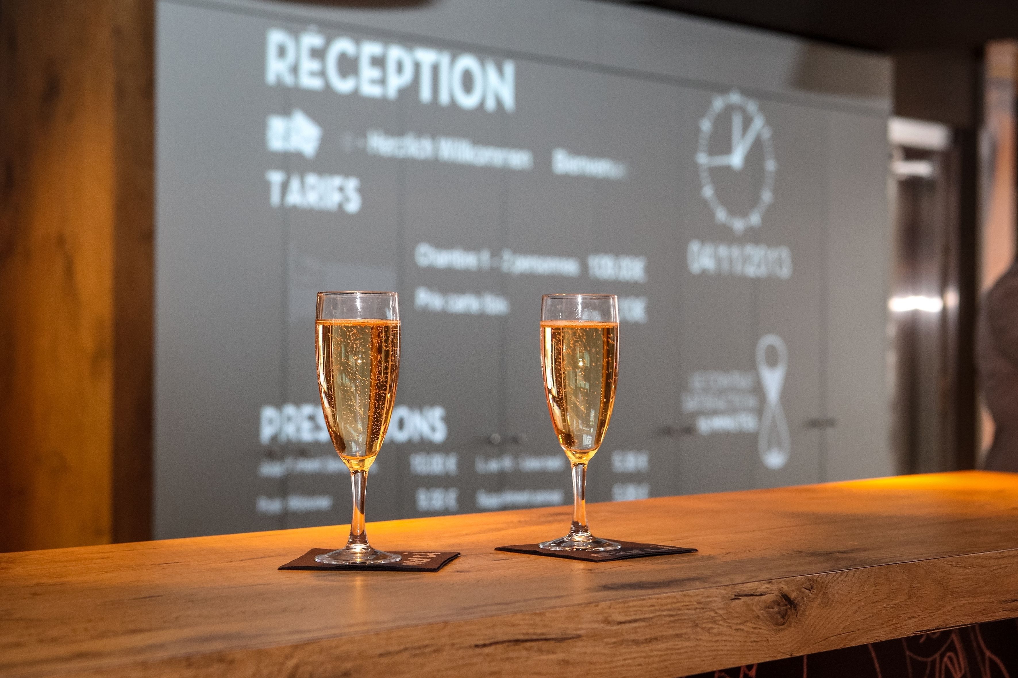Two glasses of champagne on a wooden bar counter with a reception sign in the background.